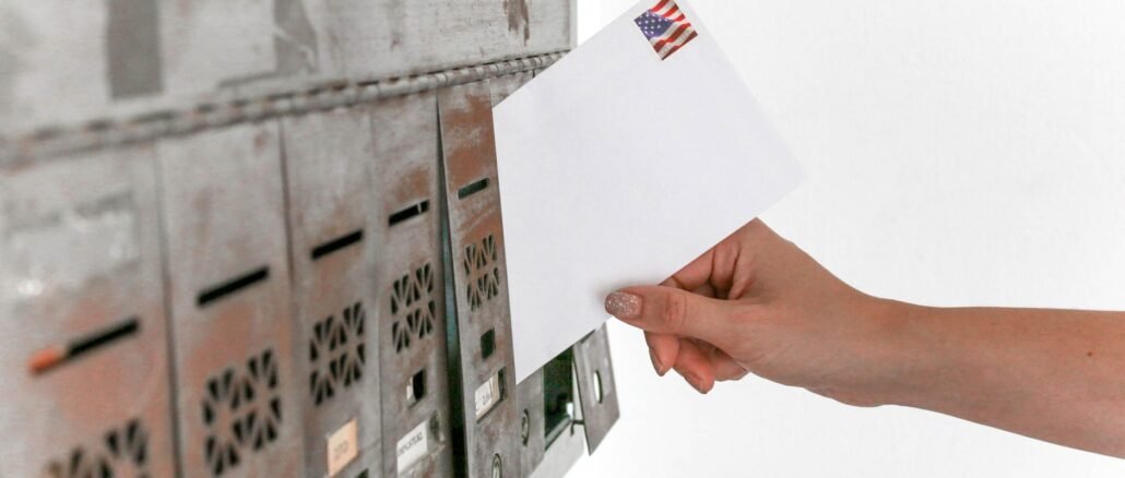 Close-up of a hand inserting a stamped envelope into a mailbox, symbolizing voting.