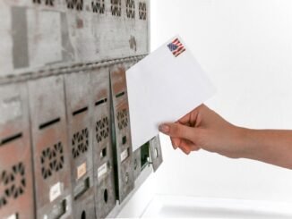 Close-up of a hand inserting a stamped envelope into a mailbox, symbolizing voting.