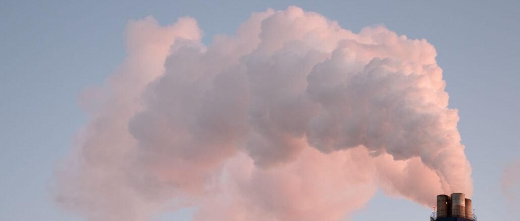 From below of clouds of smoke from industrial factory pipes polluting atmosphere against cloudless sky