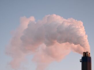 From below of clouds of smoke from industrial factory pipes polluting atmosphere against cloudless sky