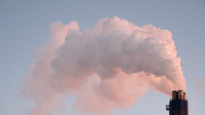 From below of clouds of smoke from industrial factory pipes polluting atmosphere against cloudless sky