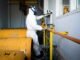 Worker in full protective suit and gas mask handles industrial pipes indoors in Indonesia.