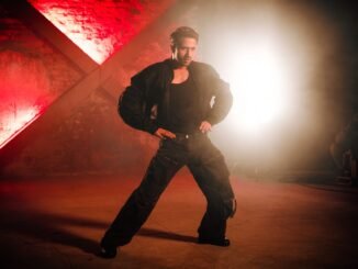 Man striking a powerful dance pose against a vibrant red backdrop with dramatic lighting.