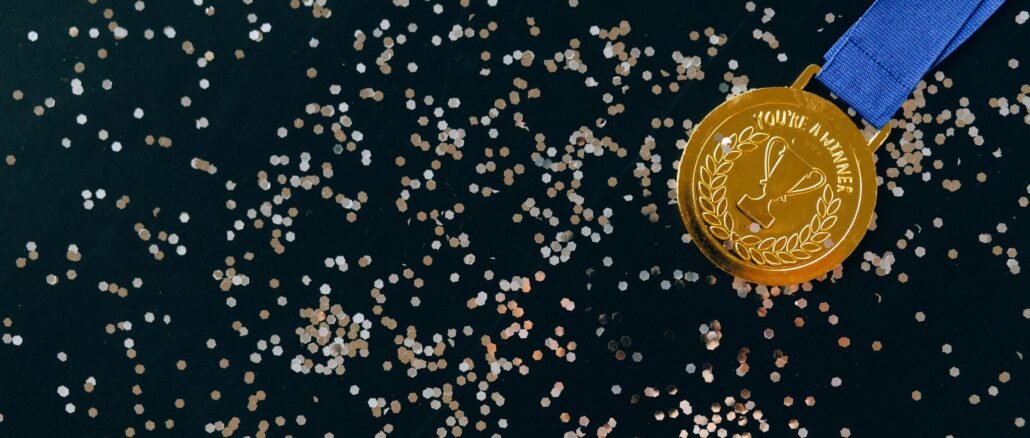 Close-up of a gold medal with blue ribbon and confetti on a black surface, symbolizing victory.