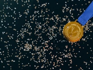 Close-up of a gold medal with blue ribbon and confetti on a black surface, symbolizing victory.
