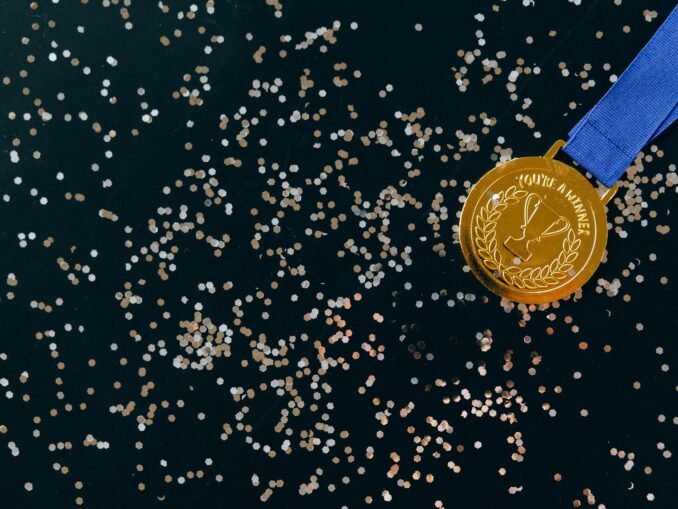 Close-up of a gold medal with blue ribbon and confetti on a black surface, symbolizing victory.