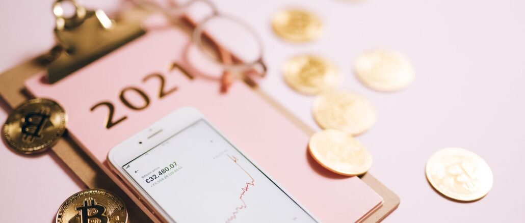 Close-up of a smartphone with crypto chart, bitcoin coins, and 2021 notepad.