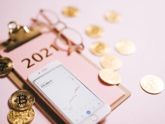 Close-up of a smartphone with crypto chart, bitcoin coins, and 2021 notepad.