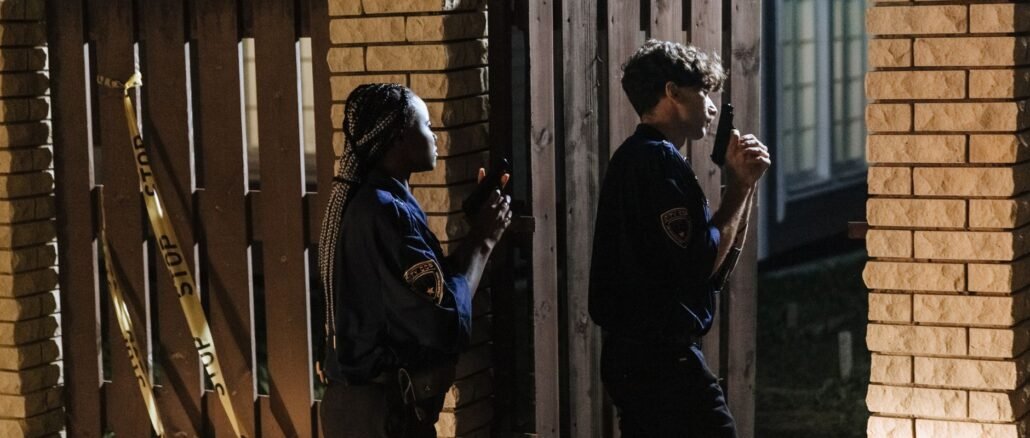 Two police officers investigate a crime scene at night, entering a house with caution.