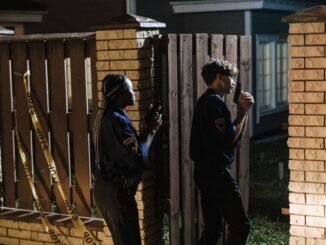 Two police officers investigate a crime scene at night, entering a house with caution.