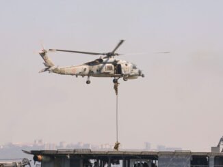 A military helicopter conducting a naval exercise with soldiers rappelling down.