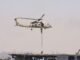 A military helicopter conducting a naval exercise with soldiers rappelling down.