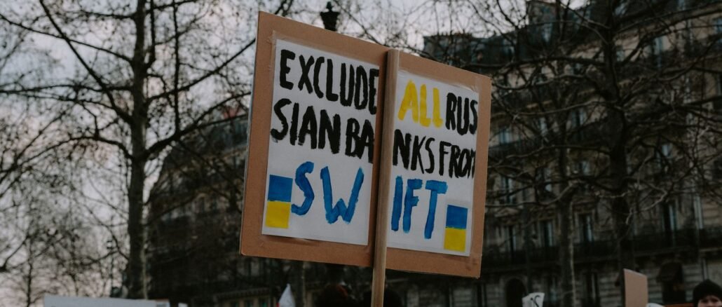Crowd gathered with placards during a protest against Russian banks in an urban setting.