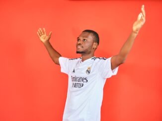 An enthusiastic football fan celebrating with arms raised in a jersey against a red background.