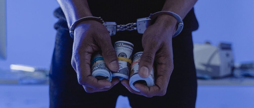 Close-up of handcuffed hands holding rolled cash, suggesting crime or arrest.