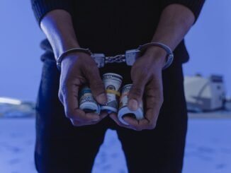 Close-up of handcuffed hands holding rolled cash, suggesting crime or arrest.