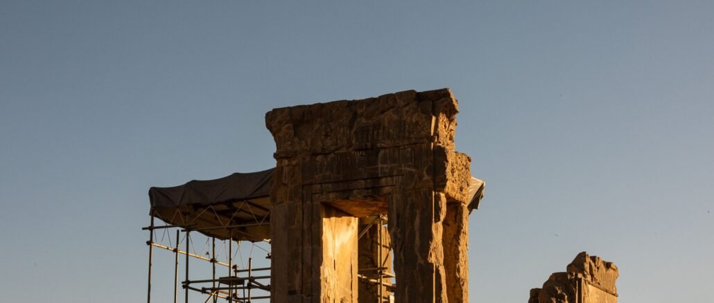 Ancient ruins of Persepolis, Iran, captured during a dramatic sunset, showcasing the architectural remnants and scaffolding.