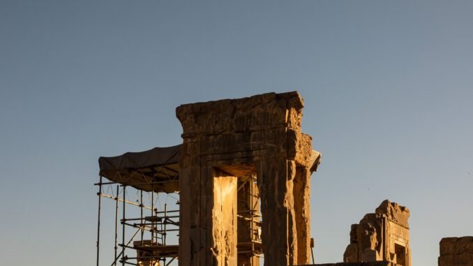 Ancient ruins of Persepolis, Iran, captured during a dramatic sunset, showcasing the architectural remnants and scaffolding.