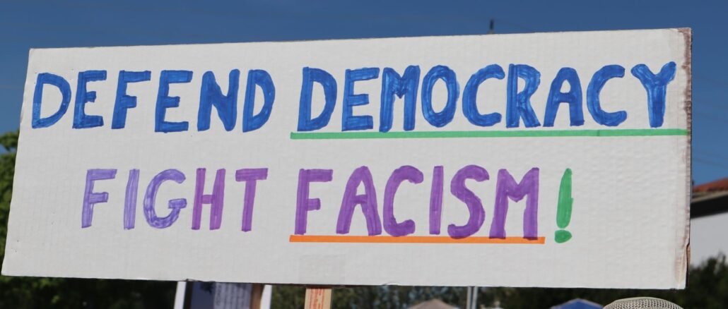 Protest sign reading 'Defend Democracy, Fight Fascism' at an outdoor rally in Elk Grove, CA.