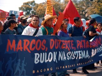 A group of protesters holding a banner during a daytime demonstration outdoors.
