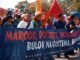 A group of protesters holding a banner during a daytime demonstration outdoors.