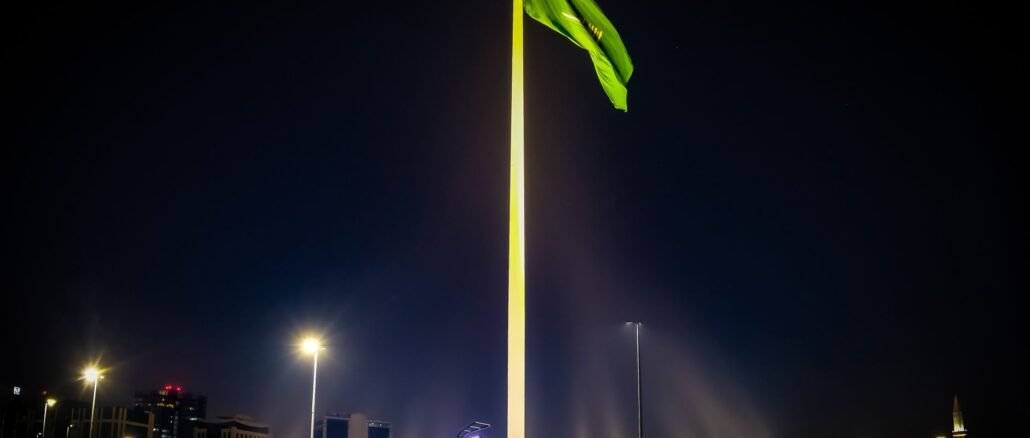 Majestic Saudi Arabian flag illuminated against the night sky, surrounded by cityscape lights in Riyadh.