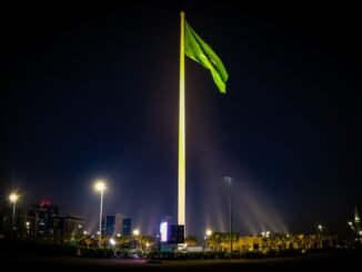 Majestic Saudi Arabian flag illuminated against the night sky, surrounded by cityscape lights in Riyadh.