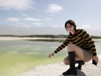 A young woman wearing sunglasses and boots poses by a scenic lake in Nanjing, China on a bright summer day.