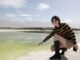 A young woman wearing sunglasses and boots poses by a scenic lake in Nanjing, China on a bright summer day.