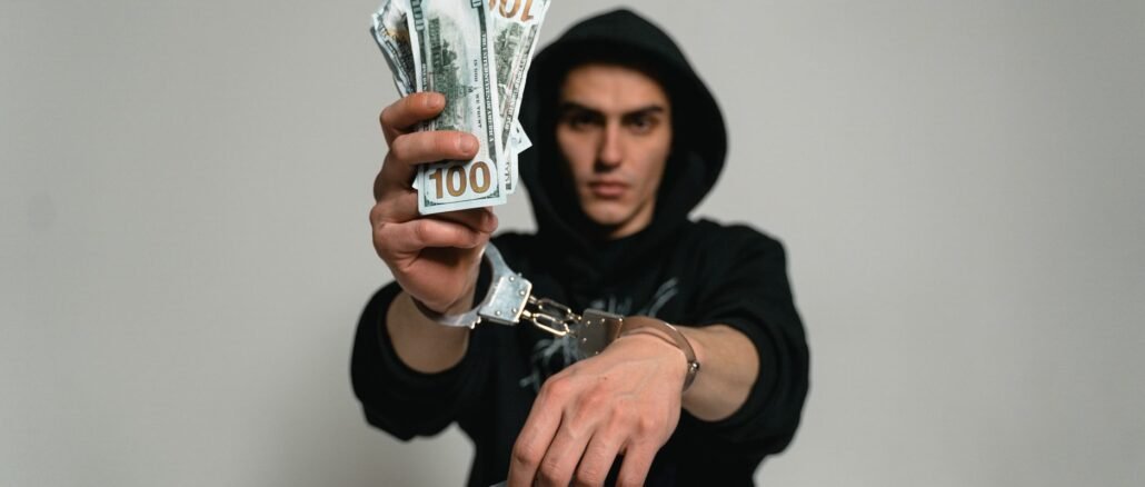 Close-up of a man in handcuffs holding cash and drugs, illustrating crime and illegal activities.