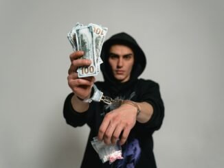 Close-up of a man in handcuffs holding cash and drugs, illustrating crime and illegal activities.